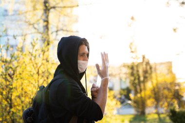 Siyah kapüşonlu, tıbbi maskeli bir adam mikropları, zehirli dumanları ve tozu önlemek için lastik eldiven giyiyor. Bakteriyel Coronavirus ya da Covid 19 salgınının önlenmesi. Küresel Karantina.