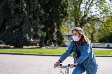 UKRAINE, KYIV - 25 Nisan 2020: Corona virüsü veya Covid 19 salgınından korunmak için tıbbi maske takan kadın sokakta bisiklet sürüyor.