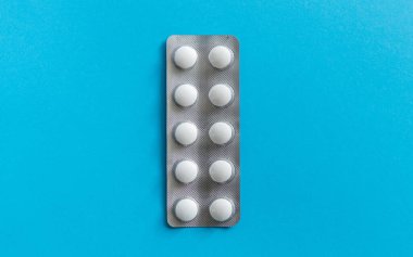 Paketteki hapların üst görüntüsü. Mavi arka planda beyaz haplar. İlaç, ilaç, ağrı kesici, tablet, ilaçlar, ilaçlar, antibiyotik, vitamin, tedavi, kapsül, doz. Eczane teması.