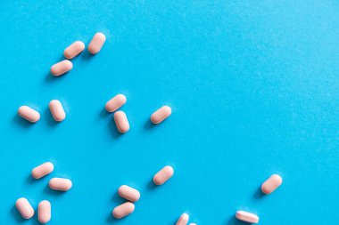 Mavi arka planda pembe haplar. İlaç, ilaç, ağrı kesici, tablet, ilaçlar, antibiyotik, vitamin, tedavi. Eczane temalı. Mavi yüzeye saçılmış hapların üst görüntüsü.