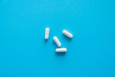 Mavi arka planda beyaz haplar. İlaç, ilaç, ağrı kesici, tablet, ilaçlar, antibiyotik, vitamin, tedavi. Eczane temalı. Mavi yüzeye saçılmış hapların üst görüntüsü.