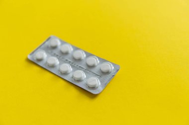 Paketteki hapların üst görüntüsü. Sarı arka planda beyaz haplar. İlaç, ilaç, ağrı kesici, tablet, ilaçlar, ilaçlar, antibiyotik, vitamin, tedavi, kapsül, doz. Eczane teması.