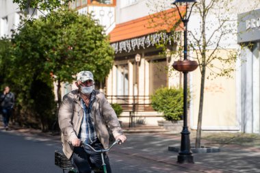 UKRAINE, KYIV - 25 Nisan 2020: Corona virüsü veya Covid 19 salgınını önlemek için tıbbi maske takan adam sokakta bisiklet sürüyor.