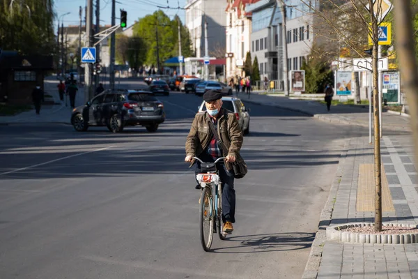 UKRAINE, KIEW - 25. April 2020: Mann mit medizinischer Maske gegen bakterielle Infektion Coronavirus oder Covid 19 Epidemie fährt Fahrrad auf der Straße. — Stockfoto