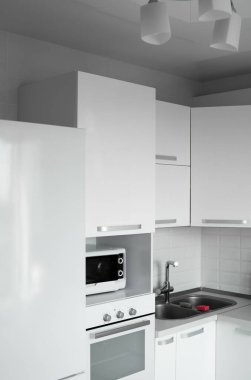 Beyaz önlüklü, rahat, beyaz bir mutfak. Modern mutfak temiz iç tasarım. Buzdolabı, mutfak fırını, mikrodalga fırın ve lavabo. Mutfak malzemeleri..
