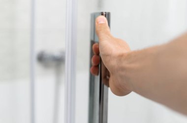 Erkek eli modern bir banyoda duş kapısını açar..