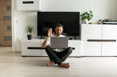 Sakallı bir adam, önünde dizüstü bilgisayarla çalışıyor ve web kamerasıyla arkadaşlarıyla, iş ortaklarıyla ya da müşterileriyle konuşuyor ve bir katta oturuyor. Evden çalışan serbest çalışan biri..