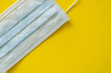 Sarı arka planda mavi tıbbi koruyucu maske var. Koronavirüsü önlemek için ağzı ve burnu kapamak için 3 katlı tıbbi maske. Bakterilerin prosedür maskesi. Coronavirus karantinası.