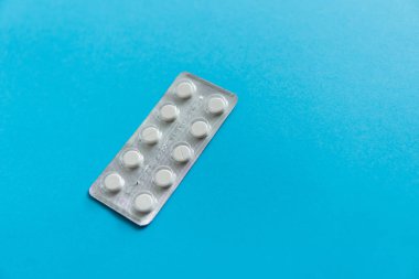 Paketteki hapların üst görüntüsü. Mavi arka planda beyaz haplar. İlaç, ilaç, ağrı kesici, tablet, ilaçlar, ilaçlar, antibiyotik, vitamin, tedavi, kapsül, doz. Eczane teması.