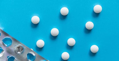 Paketten çıkarılan hapların üst görüntüsü. Mavi arka planda beyaz haplar. İlaç, ilaç, ağrı kesici, tablet, ilaçlar, ilaçlar, antibiyotik, vitamin, tedavi, kapsül, doz. Eczane