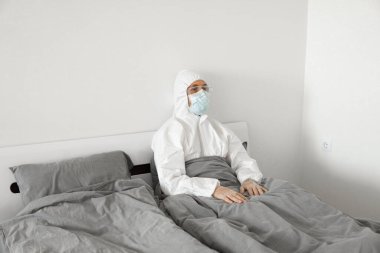 2019 'un sonundaki koronavirüs karantinasının sona ermesini bekleyen koruyucu beyaz takım elbiseli ve yüz maskeli bir adamın portresi. Kişisel tecrit.