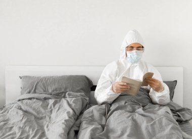 2019 sayılı kovid yüzünden yatak odasında beyaz takım elbiseli ve yüz maskeli bir adamın portresi bir kitap okuyor ve koronavirüs karantinasının sonunu bekliyor. Kişisel tecrit.