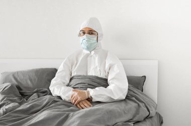 2019 'un sonundaki koronavirüs karantinasının sona ermesini bekleyen koruyucu beyaz takım elbiseli ve yüz maskeli bir adamın portresi. Kişisel tecrit.