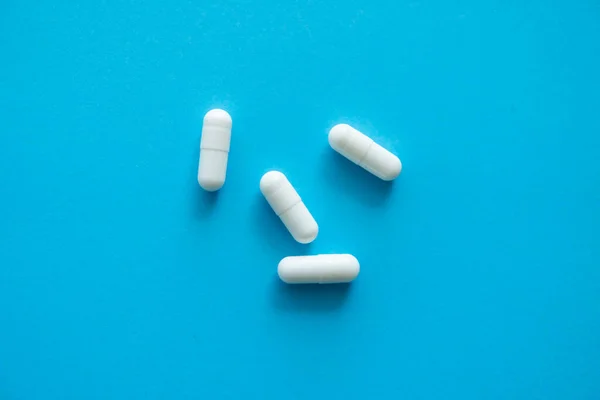 White pills on blue background. Medicine, medication, painkillers, tablet, medicaments, drugs, antibiotic, vitamin, treatment. Pharmacy theme. Top view on the pills scattered on the blue surface. — Stock Photo, Image