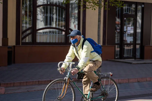 UKRAINE, KYIV - 25 kwietnia 2020: Człowiek noszący maskę medyczną zapobiegającą zakażeniu bakteryjnemu Wirus Corona lub epidemia Covid 19 jeździ na rowerze po ulicy. — Zdjęcie stockowe