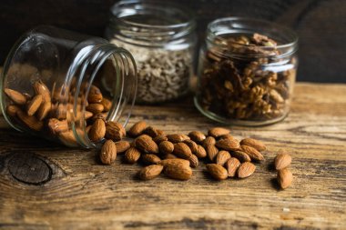 Bademler bir kavanozdan ve diğer fındıklar da arka plandaki vintage masaya saçılmış. Badem sağlıklı bir vejetaryen protein yiyeceğidir. Kırsal kesimlerdeki bademler.