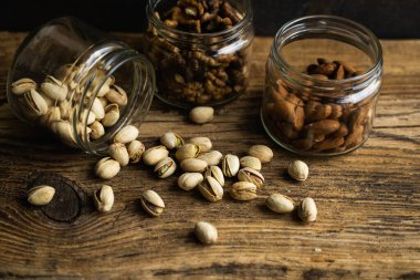 Fıstıklar bir kavanozdan ve diğer fındıklarla vintage masaya saçılmış. Pistachio sağlıklı bir vejetaryen protein yiyeceğidir. Köhne odunlarda fıstıklar.