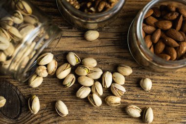 Fıstıklar bir kavanozdan ve diğer fındıklarla vintage masaya saçılmış. Pistachio sağlıklı bir vejetaryen protein yiyeceğidir. Köhne odunlarda fıstıklar.