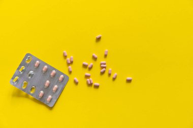 Paketten çıkarılan hapların üst görüntüsü. Sarı arka planda pembe haplar. İlaç, ilaç, ağrı kesici, tablet, ilaçlar, ilaçlar, antibiyotik, vitamin, tedavi, kapsül, doz. Eczane