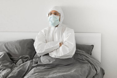 2019 'un sonundaki koronavirüs karantinasının sona ermesini bekleyen koruyucu beyaz takım elbiseli ve yüz maskeli bir adamın portresi. Kişisel tecrit.