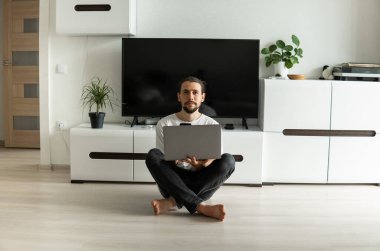 Sakallı bir adam, önünde dizüstü bilgisayarla projede çalışıyor ya da web kamerasıyla arkadaşlarıyla, iş ortaklarıyla ya da müşterileriyle konuşuyor ve bir katta oturuyor. Evden çalışan serbest çalışan biri..