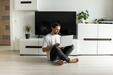 Sakallı bir adam, önünde dizüstü bilgisayarla projede çalışıyor ya da web kamerasıyla arkadaşlarıyla, iş ortaklarıyla ya da müşterileriyle konuşuyor ve bir katta oturuyor. Evden çalışan serbest çalışan biri..