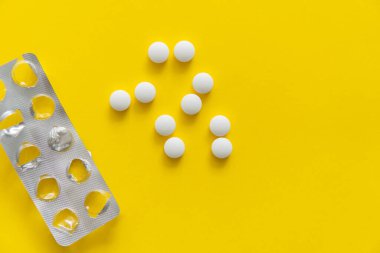 Paketten çıkarılan hapların üst görüntüsü. Sarı arka planda beyaz haplar. İlaç, ilaç, ağrı kesici, tablet, ilaçlar, ilaçlar, antibiyotik, vitamin, tedavi, kapsül, doz. Eczane