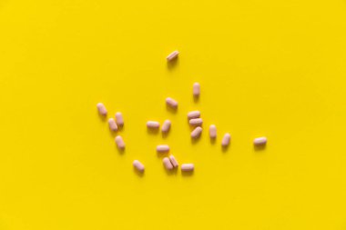 Sarı arka planda pembe haplar. İlaç, ilaç, ağrı kesici, tablet, ilaçlar, antibiyotik, vitamin, tedavi. Eczane temalı. Sarı yüzeye saçılmış hapların üst görüntüsü.