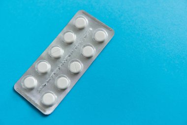 Paketteki hapların üst görüntüsü. Mavi arka planda beyaz haplar. İlaç, ilaç, ağrı kesici, tablet, ilaçlar, ilaçlar, antibiyotik, vitamin, tedavi, kapsül, doz. Eczane teması.