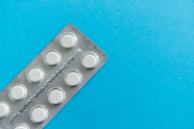 Paketteki hapların üst görüntüsü. Mavi arka planda beyaz haplar. İlaç, ilaç, ağrı kesici, tablet, ilaçlar, ilaçlar, antibiyotik, vitamin, tedavi, kapsül, doz. Eczane teması.