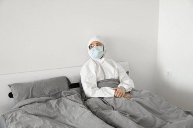 2019 'un sonundaki koronavirüs karantinasının sona ermesini bekleyen koruyucu beyaz takım elbiseli ve yüz maskeli bir adamın portresi. Kişisel tecrit.