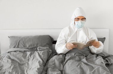2019 sayılı kovid yüzünden yatak odasında beyaz takım elbiseli ve yüz maskeli bir adamın portresi bir kitap okuyor ve koronavirüs karantinasının sonunu bekliyor. Kişisel tecrit.