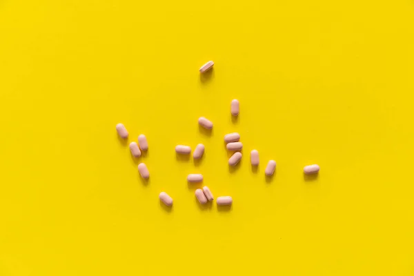 Różowe tabletki na żółtym tle. Medycyna, leki, leki przeciwbólowe, tabletki, leki, leki, antybiotyki, witaminy, leczenie. Temat apteki. Widok z góry na tabletki rozrzucone na żółtej powierzchni. — Zdjęcie stockowe
