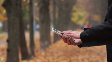 Genç adam sokakta smartphone üzerinde çalışmaktadır. Sonbahar, Sarı yapraklar, sokak.
