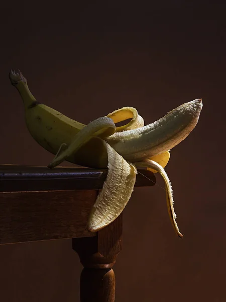 Juicy yellow white open banana, on a wooden table, with a dark background, soft light. Imitation of a Dutch kitchen still life. Mono food.