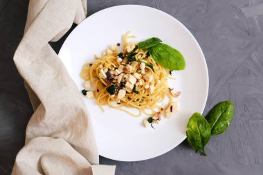 Parmesan peyniri ve bir beton zemin üzerine beyaz bir tabakta fesleğen ile makarna. Makarna peynir sos ve ıspanak ile