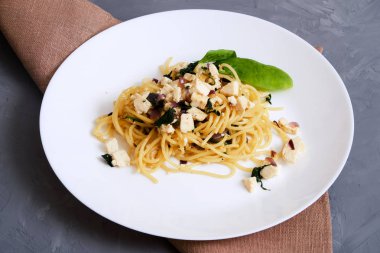 Parmesan peyniri ve bir beton zemin üzerine beyaz bir tabakta fesleğen ile makarna. Makarna peynir sos ve ıspanak ile