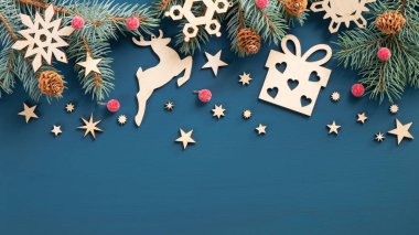 Klasik Noel çerçevesi sınırı. Köknar ağacı dalları, kırmızı böğürtlen, ahşap yıldızlar ve kar taneleri mavi arka planda yatıyordu. Üst görünüm, alanı kopyala.