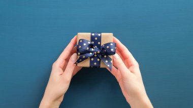 Kadının elleri mavi arka planda noktalı mavi kurdeleli hediye kutusunu tutuyor. Noel, Yeni Yıl, Sevgililer Günü ve doğum günü konsepti.