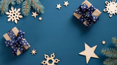Düz bir şekilde Noel hediye kutuları ve koyu mavi arka planda ahşap el yapımı süslemeleri olan köknar ağacı dalları uzanıyordu. Xmas çerçeve, fotokopi alanı olan yeni yıl afişi. Üst görünüm.