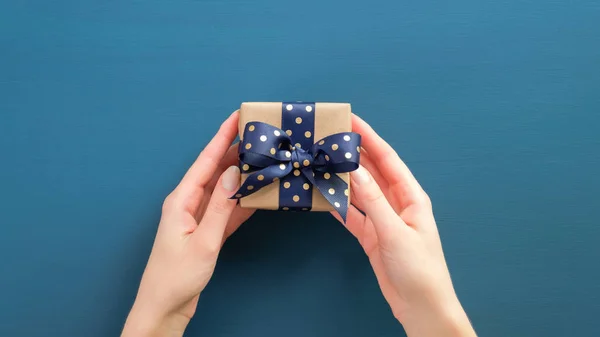 Woman hands holding gift box with dotted blue ribbon over blue background. Christmas, New Year, Valentine's day and birthday concept. — Stock Photo, Image