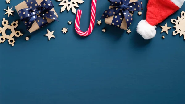 Natal quadro fronteira feriado de caixas de presente retro, cana-de-açúcar, chapéu de Papai Noel, flocos de neve artesanais de madeira sobre fundo azul escuro. Xmas banner mockup com espaço de cópia. Deitado plano, vista superior — Fotografia de Stock