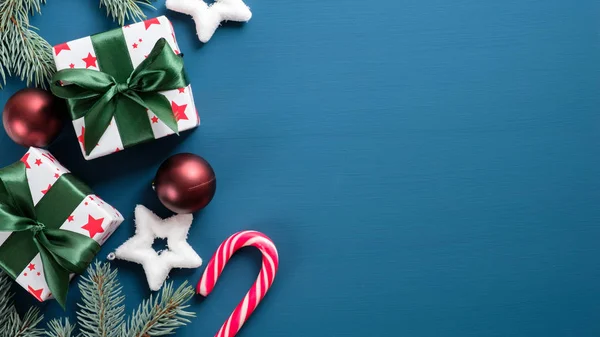 맨 위에서 보는 빈티지 크리스마스 선물은 파란색 배경에 복사 공간 이 있는 것이다. 납작 하게 놓인 선물 상자에 녹색 리본 활, 소나무 가지, 공, 별, 사탕등 이 있었습니다. 새해 깃발 흉내, 엽서 템플릿 — 스톡 사진