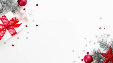 Üst manzara Noel hediyesi ve beyaz arka planda fotokopi alanı olan dekorasyonlar. Kırmızı kurdeleli düz bir hediye kutusu, Noel ağacı dalları, toplar, yıldız ve konfeti. Yeni yıl tebrik kartı