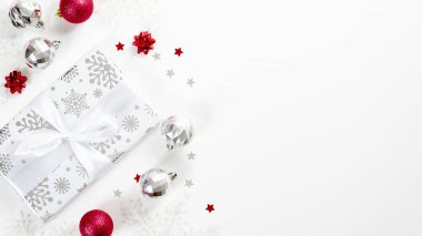 Şık bir Noel hediyesi kıpkırmızı ve gümüş toplar ve beyaz arka planda süslemeler. Düz konum, üst görünüm, kopyalama alanı. Noel afişi modeli, kış tatili tebrik kartı şablonu