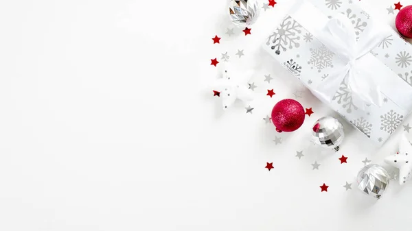 Caixa de presente de Natal de prata elegante com laço de fita e decorações vermelhas de Natal no fundo branco com espaço de cópia. Feriados de inverno modelo de cartão de saudação, Ano Novo banner mockup — Fotografia de Stock