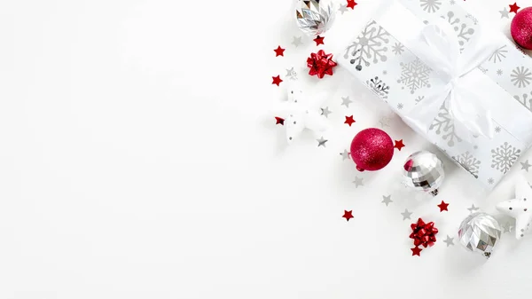 Top view Χριστουγεννιάτικο δώρο και ασημένια και κόκκινα στοιχεία διακόσμησης σε λευκό φόντο. Flat lay κουτί δώρου με κορδέλα τόξο, μπάλες, αστέρια, κομφετί. Χριστούγεννα, χειμερινές διακοπές, την έννοια της Πρωτοχρονιάς. — Φωτογραφία Αρχείου