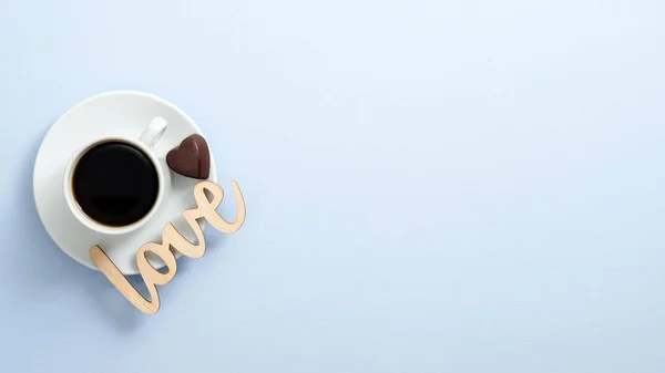 Top view coffee cup espresso with heart shaped chocolate candy and wooden word sign "Love" on blue background. Flat lay, overhead. Valentine's day concept. — Stock Photo, Image