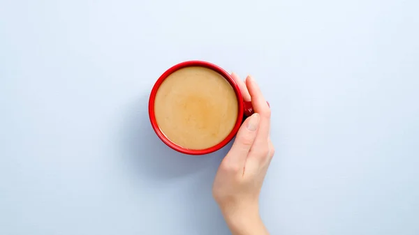 Kvinna hand hålla latte kaffekopp på blå bakgrund. Platt låg, ovanifrån, ovanifrån. — Stockfoto