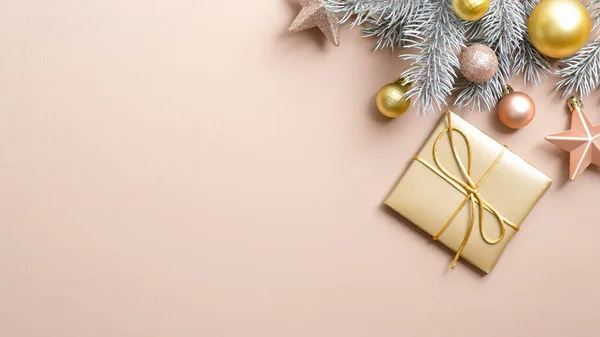 Altın Noel hediye kutusu ve pastel bej arka planda süslemeleri olan Xmas afişi. Düz gümüş çam ağacı dalında altın yıldızlar ve pembe toplar vardı. Kopyalama alanı olan üst görünüm.